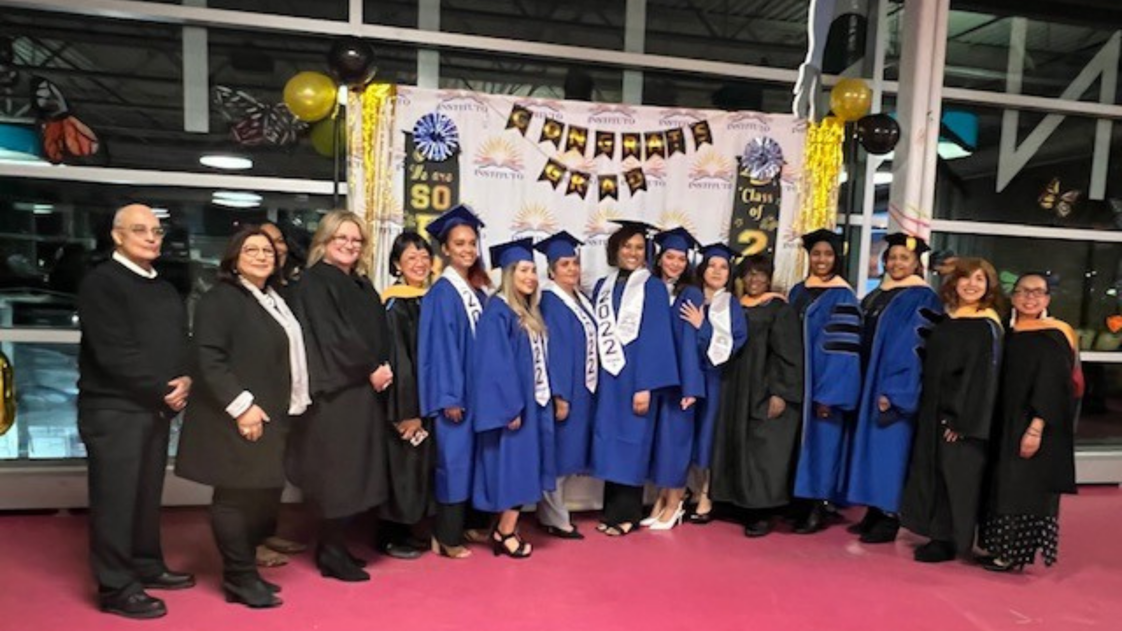 Class of 2022 Instituto College Graduates, IDPL Staff, and President Maria Pesqueira pose in front of graduation banner